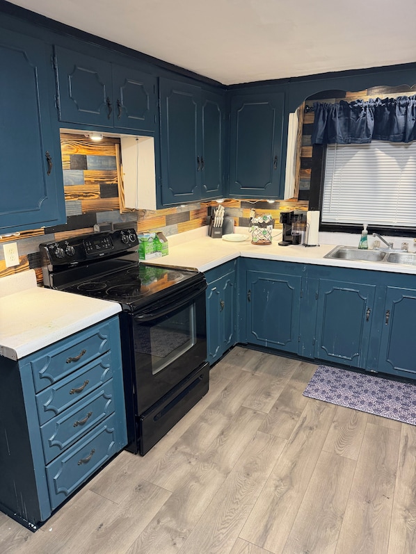 Une cuisine avec des meubles de couleur bleue, une cuisinière noire et une fenêtre avec des stores.