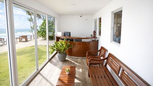 A spacious room with a wooden reception desk, a potted plant, and a seating area with wooden benches. - Noa Sands Talpe  by Ceylon Vistas (Talpe)