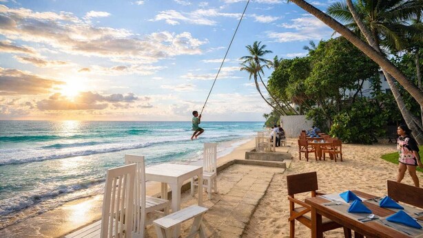 A beachside restaurant with outdoor seating, palm trees, and a view of the ocean. - Noa Sands Talpe  by Ceylon Vistas (Talpe)