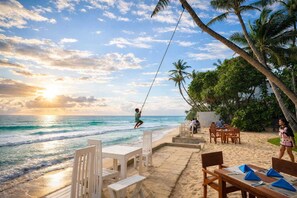A beachside restaurant with outdoor seating, palm trees, and a view of the ocean. - Noa Sands Talpe  by Ceylon Vistas (Talpe)