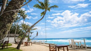 A beachside restaurant with outdoor seating, palm trees, and a view of the ocean. - Noa Sands Talpe  by Ceylon Vistas (Talpe)