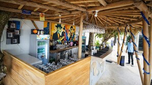 A rustic bar area with wooden beams, a mural, and a refrigerator stocked with beverages. - Noa Sands Talpe  by Ceylon Vistas (Talpe)
