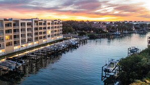 Hotel aan het waterwater met meerdere balkons, een jachthaven met boten en uitzicht op de zonsondergang.