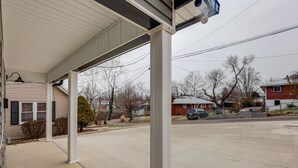 A covered porch with a concrete floor, a lamp post, and a view of a residential street with houses and a parked car.