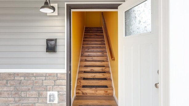 A wooden staircase with a yellow wall and a white door at the bottom.