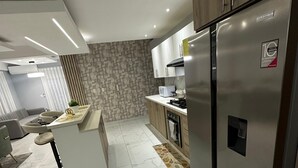 Eine moderne Küche mit Edelstahlkühlschrank, Marmorboden und einer integrierten Kochinsel mit Sitzgelegenheiten.