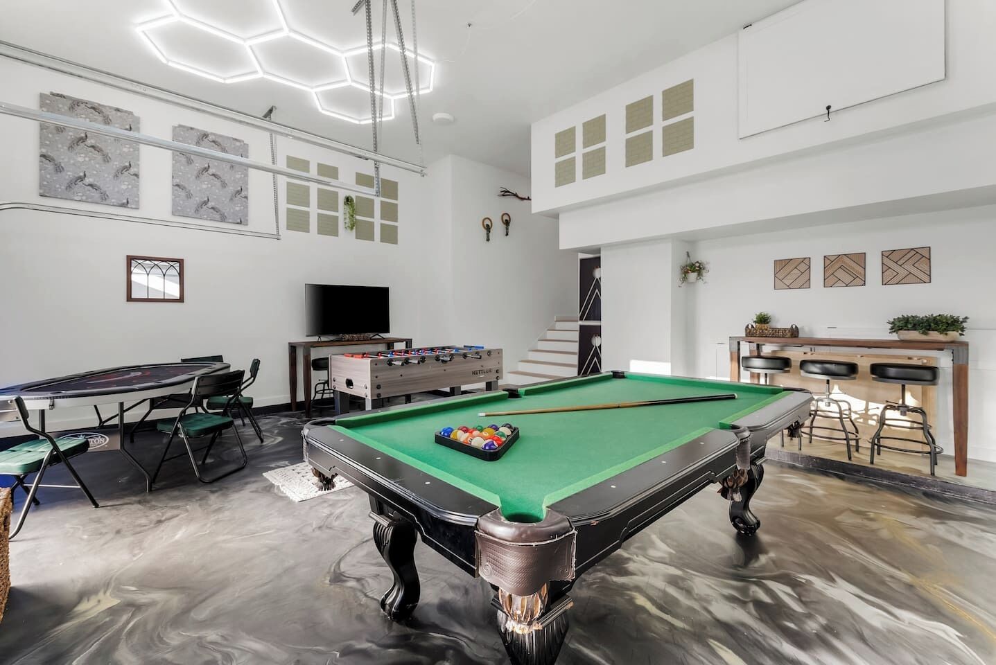 A spacious room with a pool table, foosball table, and a bar area.