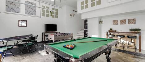 A spacious room with a pool table, foosball table, and a bar area.