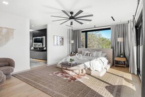 A modern bedroom with a large bed, a ceiling fan, a view of the outdoors, and a separate bathroom area. - Modern Hilltop Retreat with Pool Near Downtown (Austin)