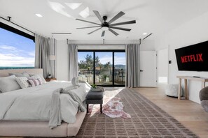 A modern bedroom with a large bed, a ceiling fan, a TV, and a balcony with a view. - Modern Hilltop Retreat with Pool Near Downtown (Austin)