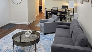 Un salon avec un canapé gris, une table basse et un coin repas comprenant une table et des chaises.