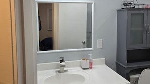 Une salle de bain avec un lavabo blanc, un miroir et un meuble.