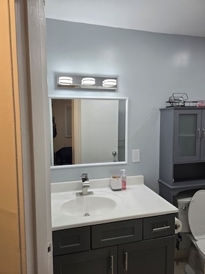 Une salle de bain avec un lavabo blanc, un miroir et un meuble.