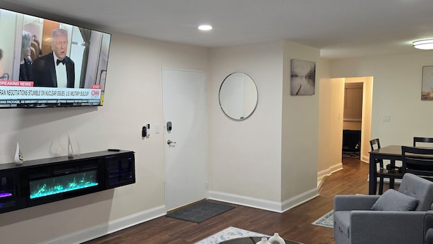 Un salon moderne avec un téléviseur à écran plat fixé au mur, une cheminée avec une façade en verre, une table basse ronde et un canapé gris.