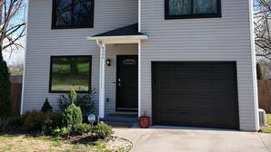 Een tweelaags huis met een garage, een zwarte voordeur en een klein portiek.