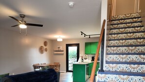 Een ruime woonkamer met een donkerblauwe bank, een plafondventilator en een trap met betegelde tredes.