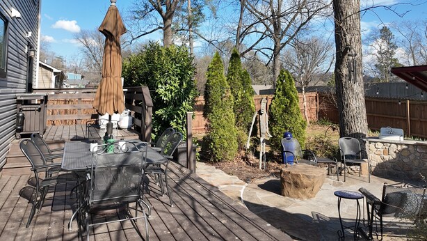Een houten terras met een tafel en stoelen, omringd door bomen en een houten hek.