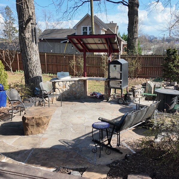 A backyard patio with stone flooring, a barbecue grill, outdoor seating, and a covered area.