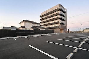 Un estacionamiento con espacios delimitados y un edificio de varios pisos y balcones.