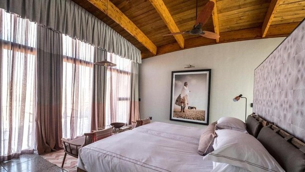 A bedroom with a large bed, wooden ceiling beams, a framed picture on the wall, and a window with curtains. - The Desert Grace, Gondwana Collection Namibia (pty (Sesriem)