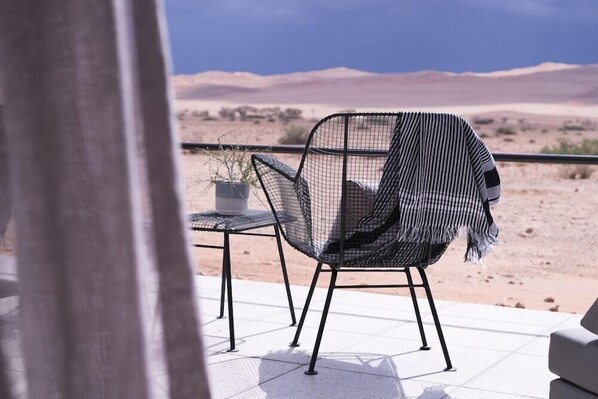 Un espacio de estar moderno al aire libre con una silla y mesa de metal, con vistas a un paisaje desértico.