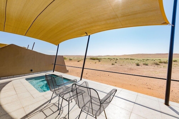 Ein Poolbereich mit Blick auf eine Wüstenlandschaft, ein überdachter Sitzbereich und ein Tisch am Pool.
