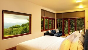 A bedroom with a large bed, a sofa, and a view of a forest through the windows. - Kandy Knightsdale Villa (Menikhinna)