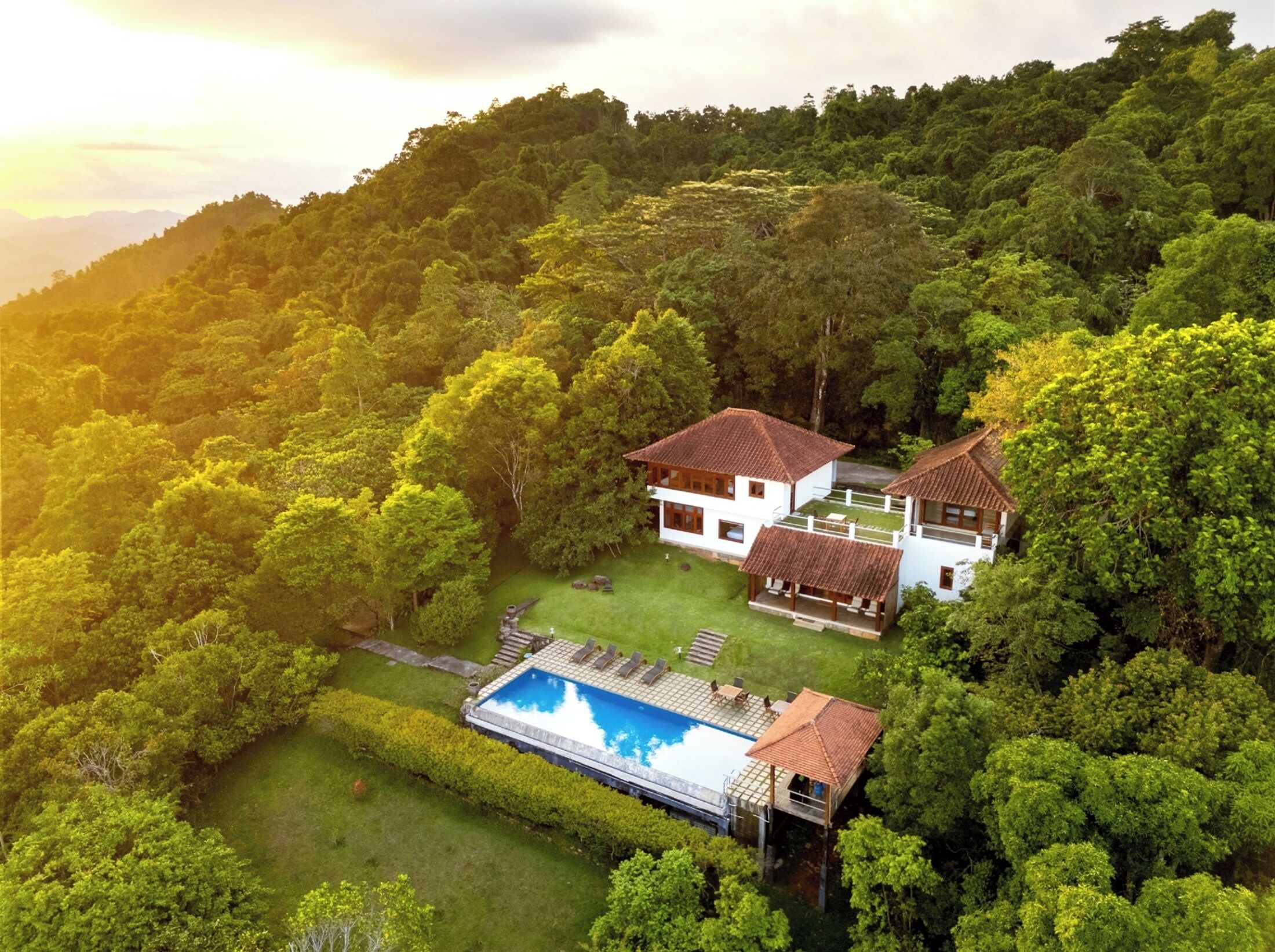 A two-story house with a swimming pool surrounded by lush greenery.