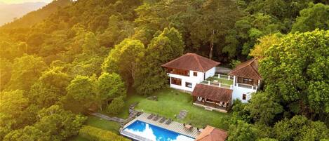 A two-story house with a swimming pool surrounded by lush greenery.