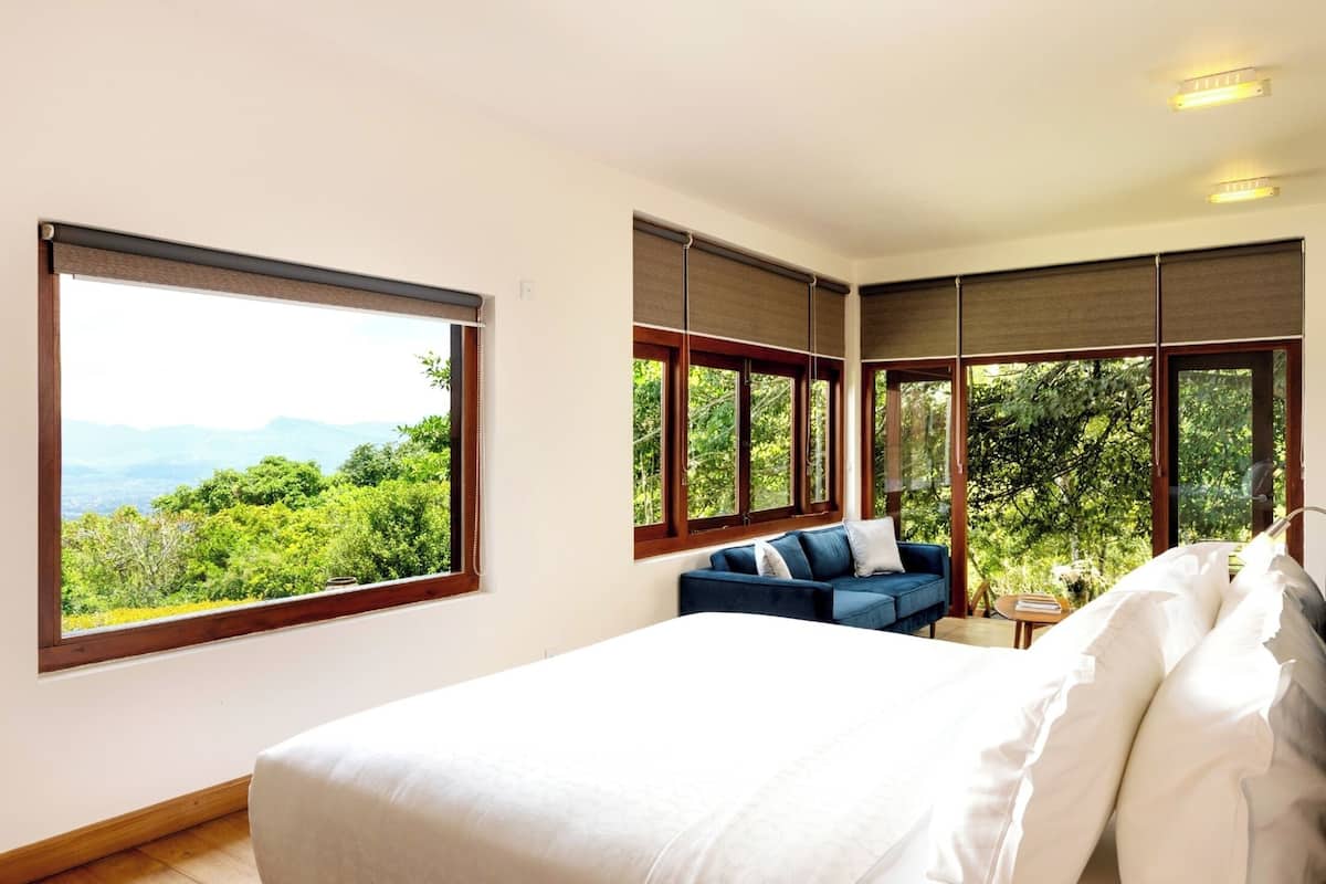 Une chambre dotée d’un grand lit, d’un canapé bleu et de nombreuses fenêtres donnant sur un paysage verdoyant et montagneux.