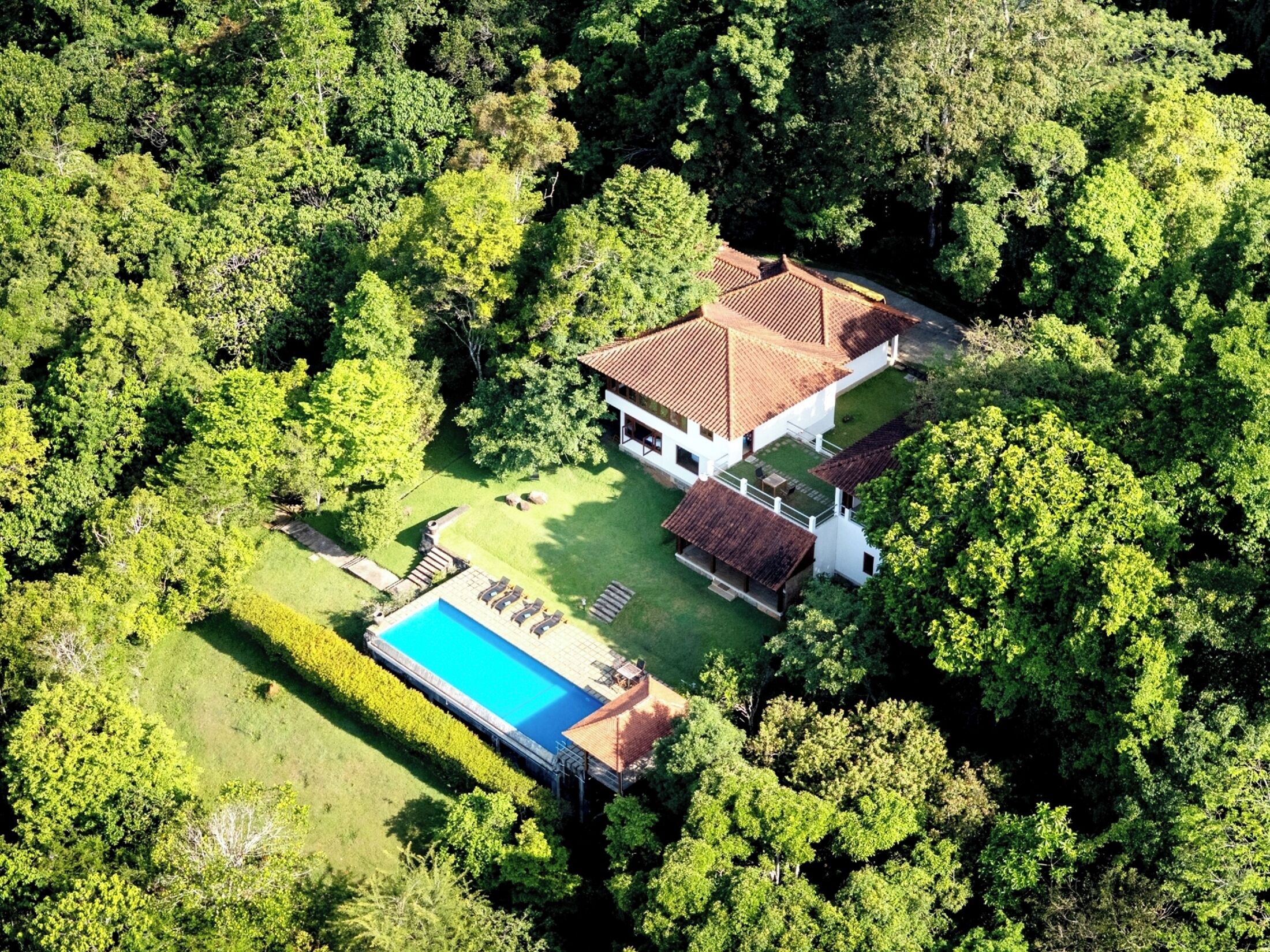Vista aérea de una casa rodeada de abundante vegetación, con piscina y césped cuidado.