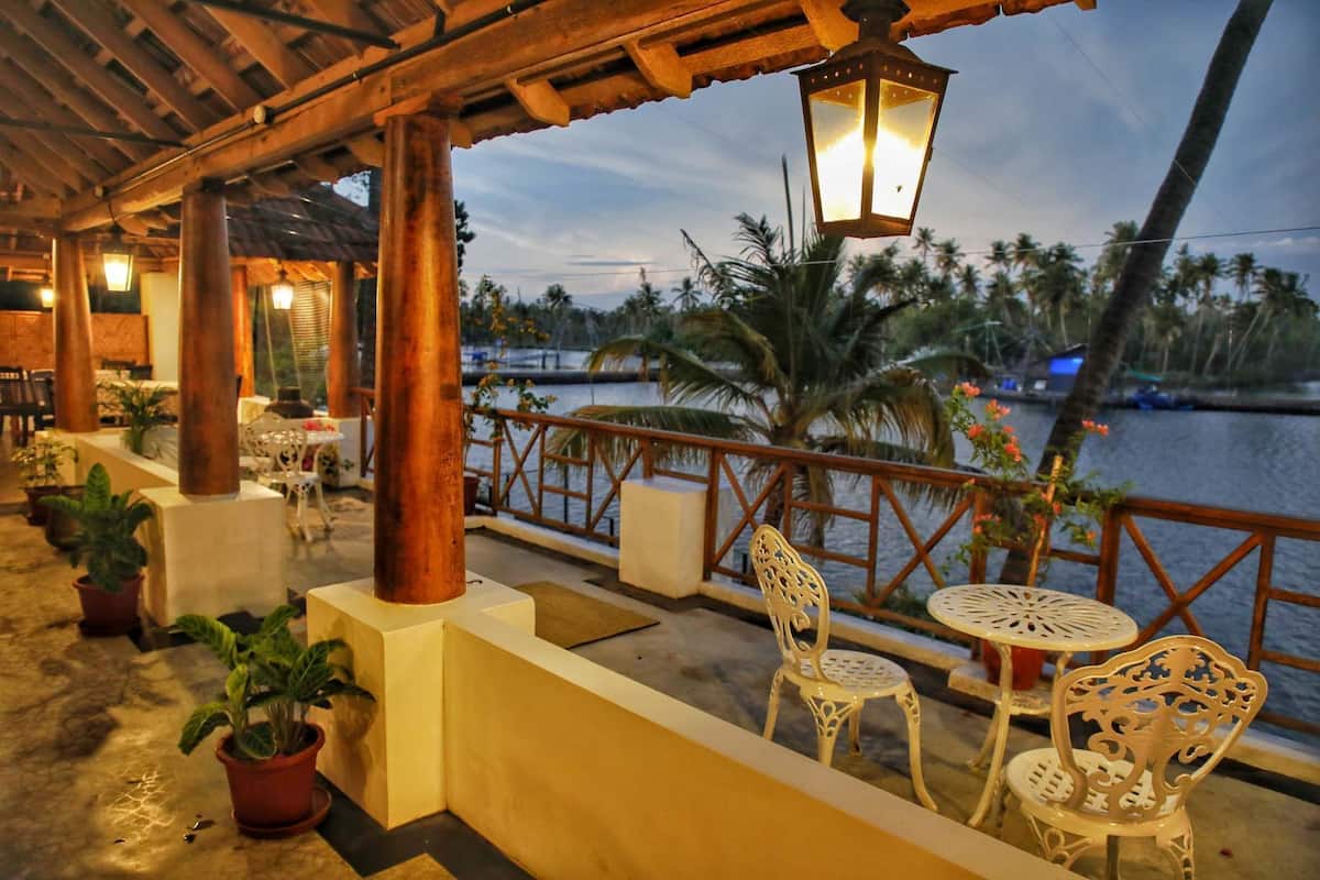 A covered outdoor seating area with tables and chairs, a railing overlooking a body of water, and a lamp hanging above.