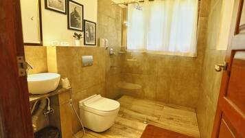 A bathroom with a toilet, sink, shower, and a wooden floor.