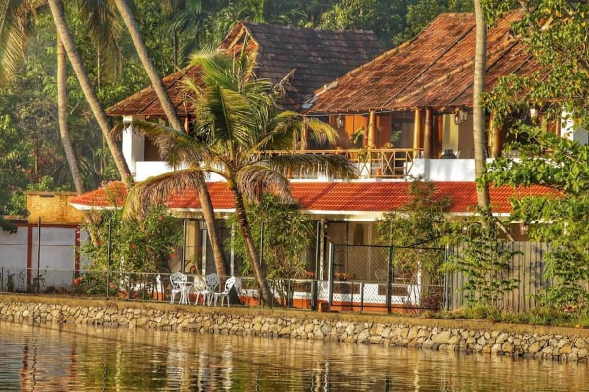 A two-story house with a red roof, surrounded by a stone wall and palm trees.
