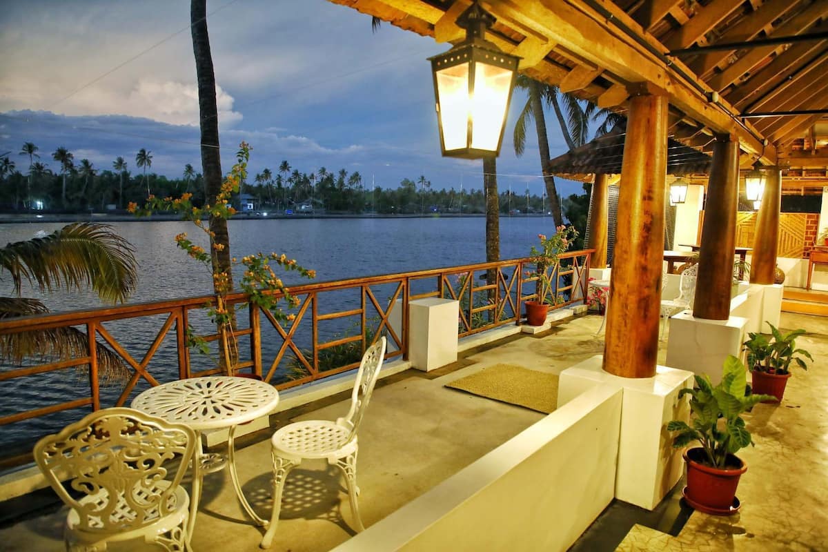 A covered outdoor seating area with a view of a lake and palm trees.