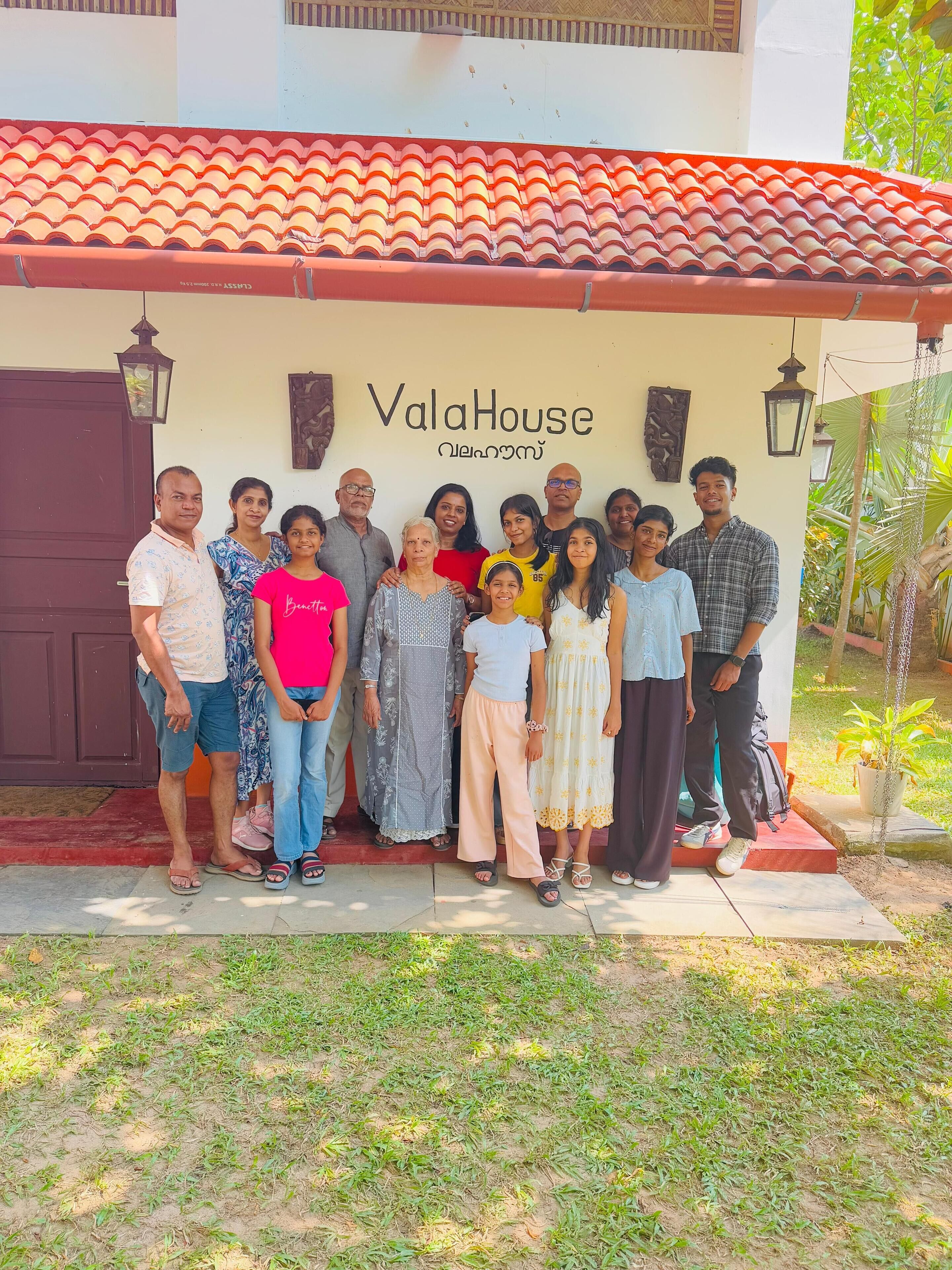 A group of people posing in front of a building with a tiled roof and a sign that reads "ValaHouse."