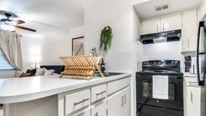 A modern kitchen with white cabinetry, a black stove, and a wooden rack on the countertop. - Cozy Comfort Getaway North ATX Studio Convenient Easy Major City Access (Austin)