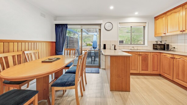 Una cucina moderna con mobili in legno, un'area pranzo con tavolo e sedie, e vista attraverso la porta in vetro.