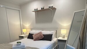Una camera da letto ordinata con un letto, comodini, una ventola a soffitto, uno specchio e uno scaffale con oggetti decorativi.
