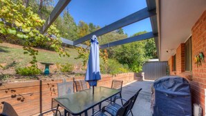 Una veranda riparata con tavolo e sedie, un barbecue coperto e un muro in mattoni.