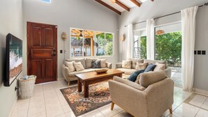 A spacious living room with a large sofa set, a wooden coffee table, and a TV on the wall. - 4BR Tropical Retreat • Pool • Beach • Golf Cart (Playa Potrero, Santa Cruz)