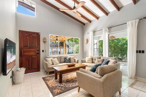 A spacious living room with a large sofa set, a wooden coffee table, and a TV on the wall. - 4BR Tropical Retreat • Pool • Beach • Golf Cart (Playa Potrero, Santa Cruz)