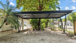 A covered outdoor area with a gravel ground, a palm tree, and a fenced property. - 4BR Tropical Retreat • Pool • Beach • Golf Cart (Playa Potrero, Santa Cruz)