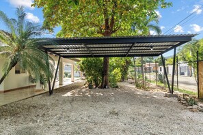 A covered outdoor area with a gravel ground, a palm tree, and a fenced property. - 4BR Tropical Retreat • Pool • Beach • Golf Cart (Playa Potrero, Santa Cruz)