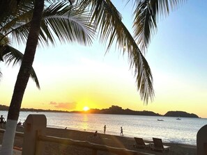 A beach scene with palm trees, a sunset, and a calm sea. - 4BR Tropical Retreat • Pool • Beach • Golf Cart (Playa Potrero, Santa Cruz)