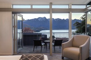 Uma varanda com vista para montanhas e um lago, equipada com uma cadeira e uma mesa.