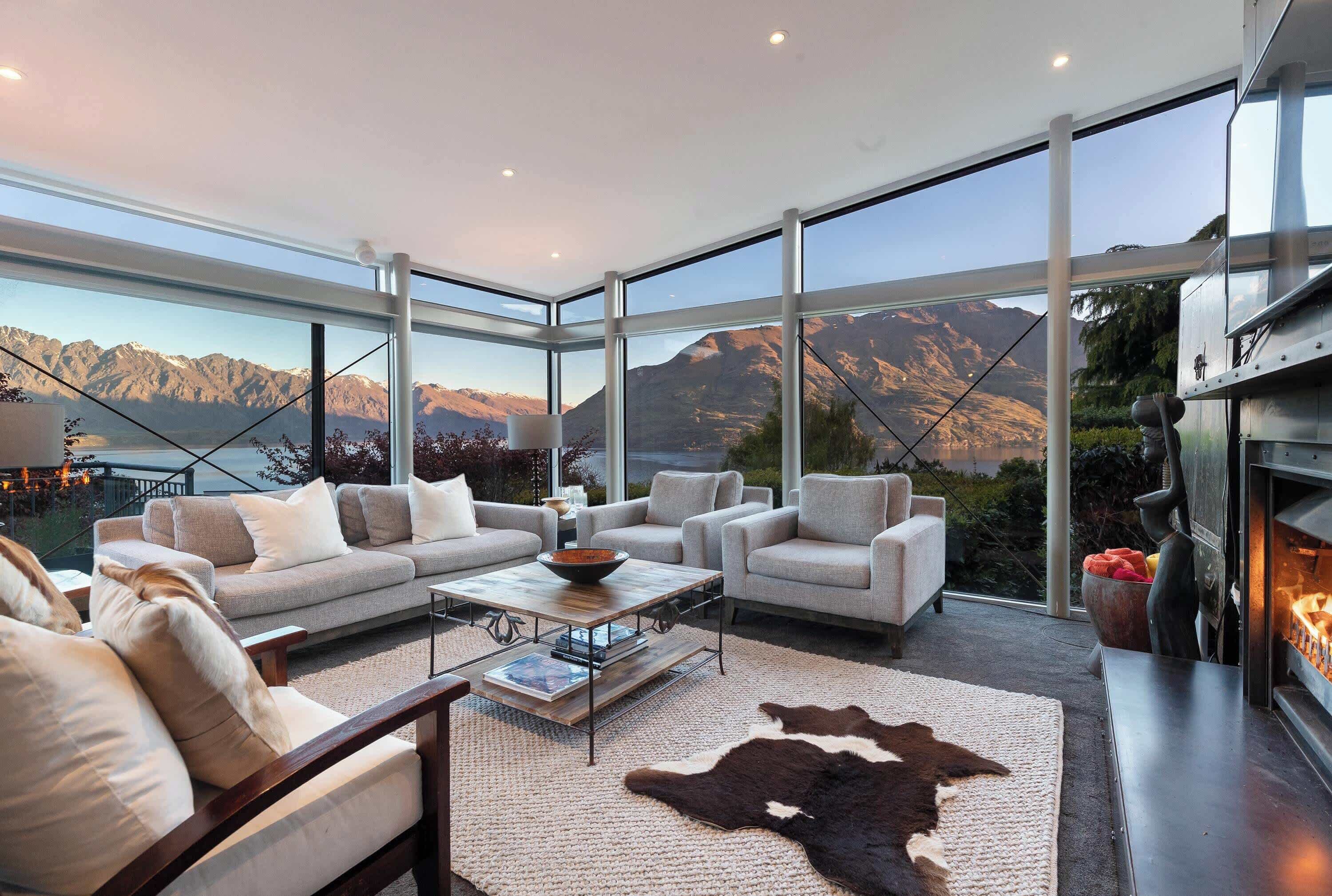 A modern living room with a large glass wall, a fireplace, and a leather rug.