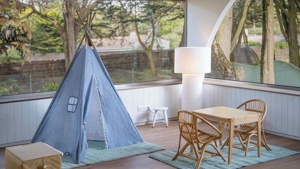 Une pièce chaleureuse avec une tente bleue, une table avec des chaises, une lampe et une fenêtre donnant sur la verdure.