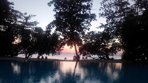 Piscina com vista para o pôr do sol, cercada por árvores e cadeiras de descanso.