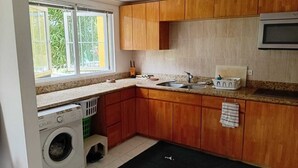 Cozinha compacta com armários de madeira, micro-ondas embutido, pia e máquina de lavar.